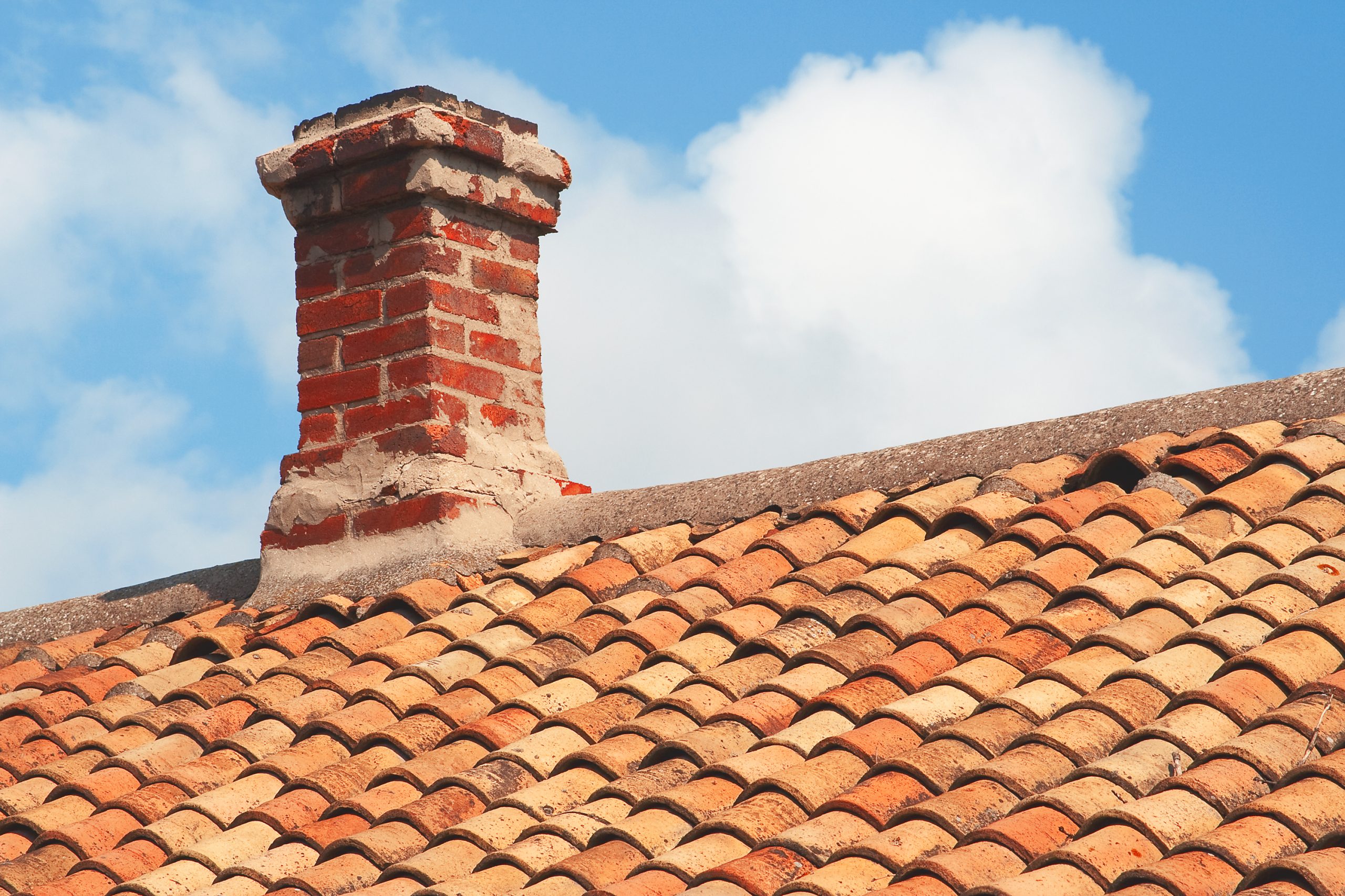 Tile roof with brick chimney against a blue sky